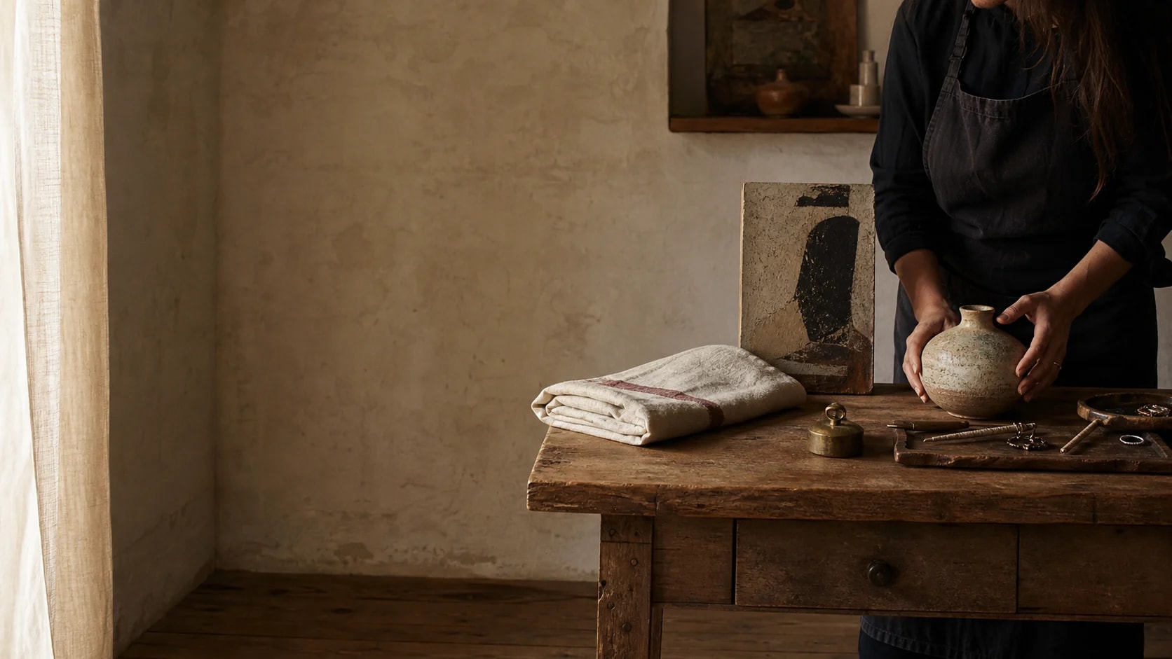 An artisan arranging handmade objects, art, linen, and jewelry in a quiet studio